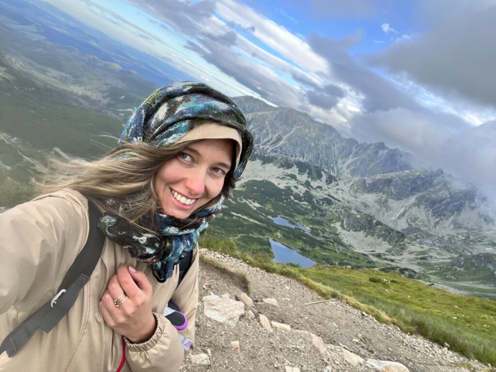 Image shows a girl showing the view from the top of the mountain with lakes and more mountains in the background